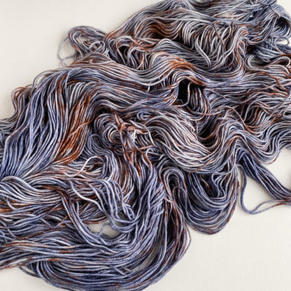 Yarn unfurled and tossed onto a white background. The yarn has been dyed with blue and brown dyes