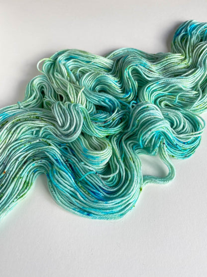 Blue and green yarn unfurled from a hank and lying across a white background