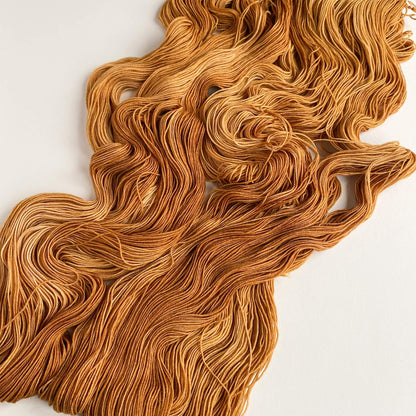 Brown coloured yarn has been unfurled from its skein and lies across a white table. 