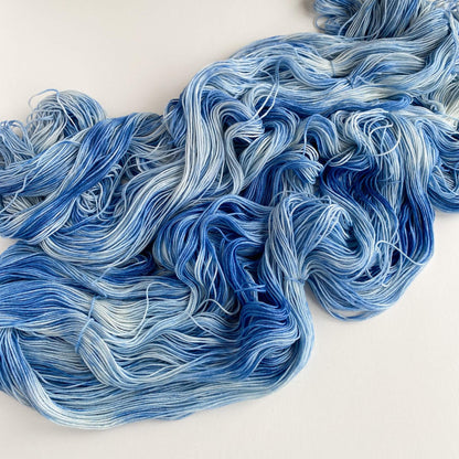 Blue hand dyed yarn has been unfurled from its skein and tossed on a white table top.