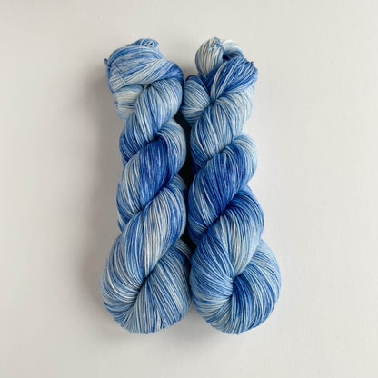 Two skeins of hand dyed yarn on a white table top. The yarn has been dyed with blue dyes. 