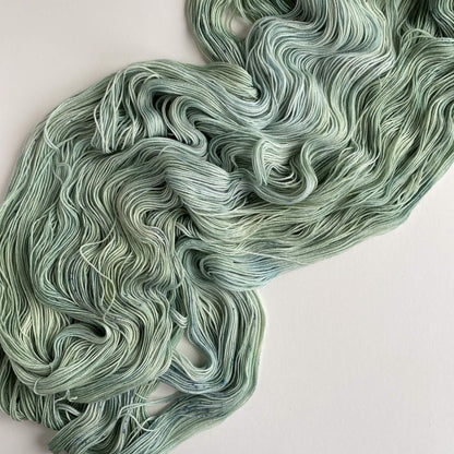 Hand dyed yarn dyed in a green colourway and lies unfurled across a white table top. 