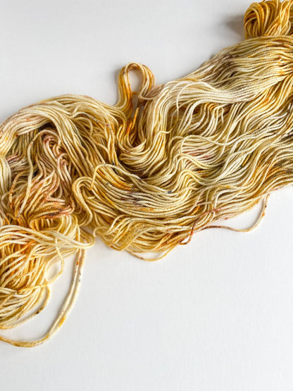 Yarn has been unfurled from a skein and tossed onto a table. It has been dyed with orange and brown dyes. 