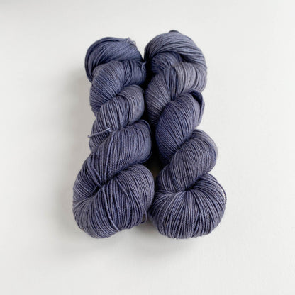 Two skeins of hand dyed yarn on a white table top. The yarn has been dyed with grey dyes. 