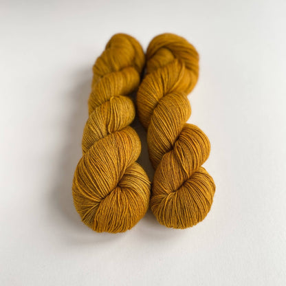 Two skeins of hand dyed yarn on a white table top. The yarn has been dyed with brown and orange dyes. 