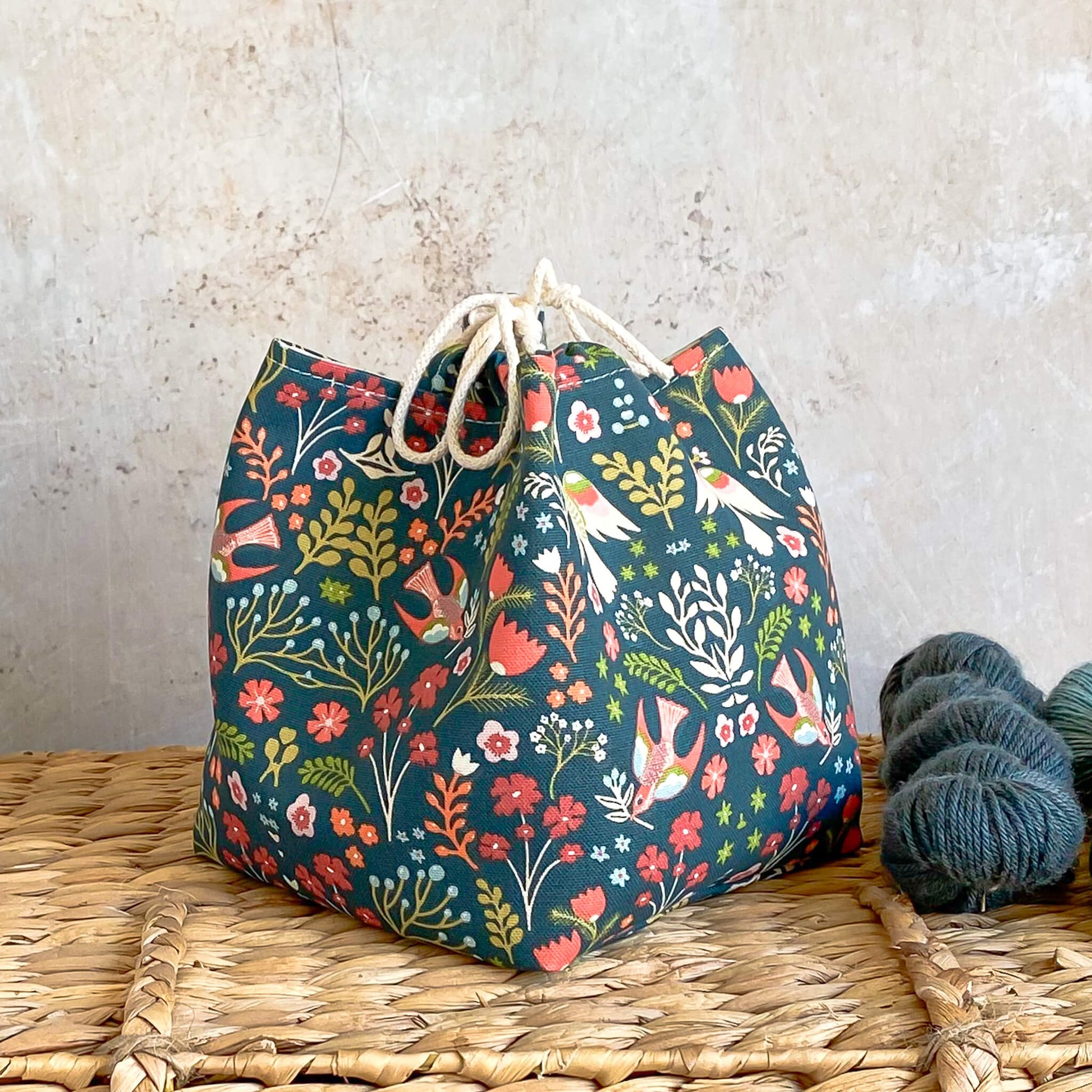 A side on view of a green nature themed project bag. The bag is based on the Japanese rice bag design and is intended to hold kmnitting and crochet projects. 