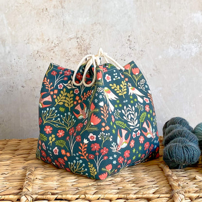 A side on view of a green nature themed project bag. The bag is based on the Japanese rice bag design and is intended to hold kmnitting and crochet projects. 