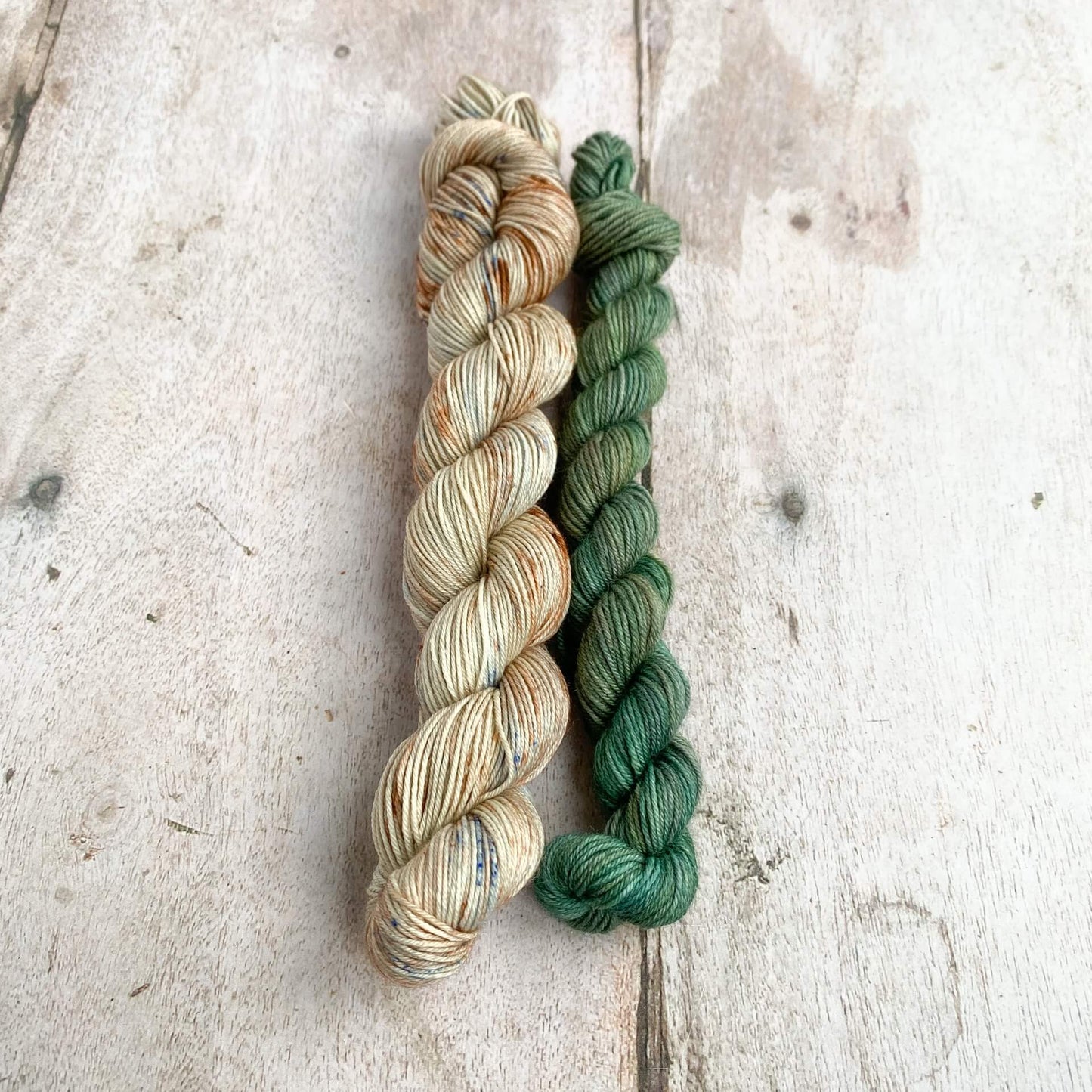 Two skeins of yarn in colours of brown, speckled blue and green sit on a wooden table. 