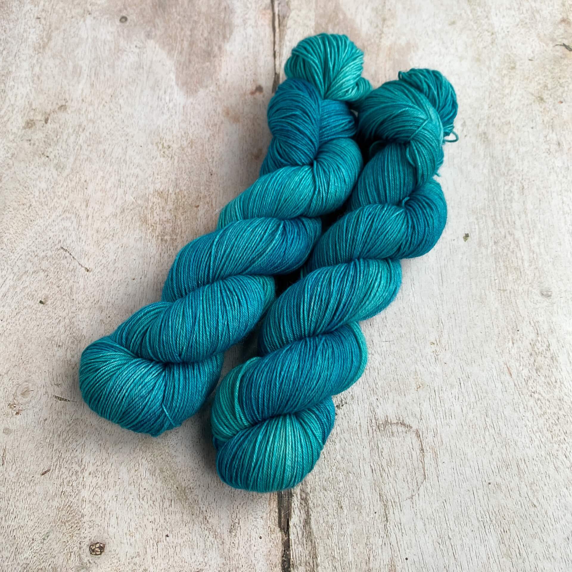 Two skeins of a tonal teal blue yarn sit together on a wooden table. 