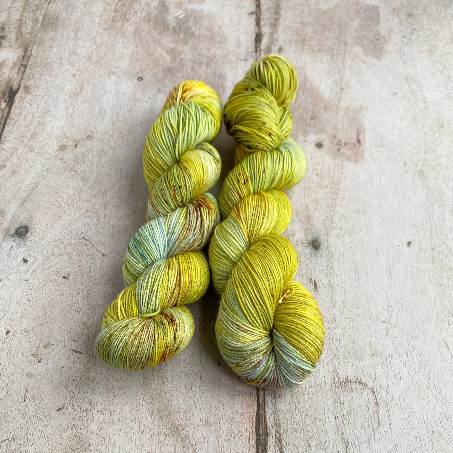 Two skeins of golden green and light blue hand dyed yarn sit together on a wooden table. 