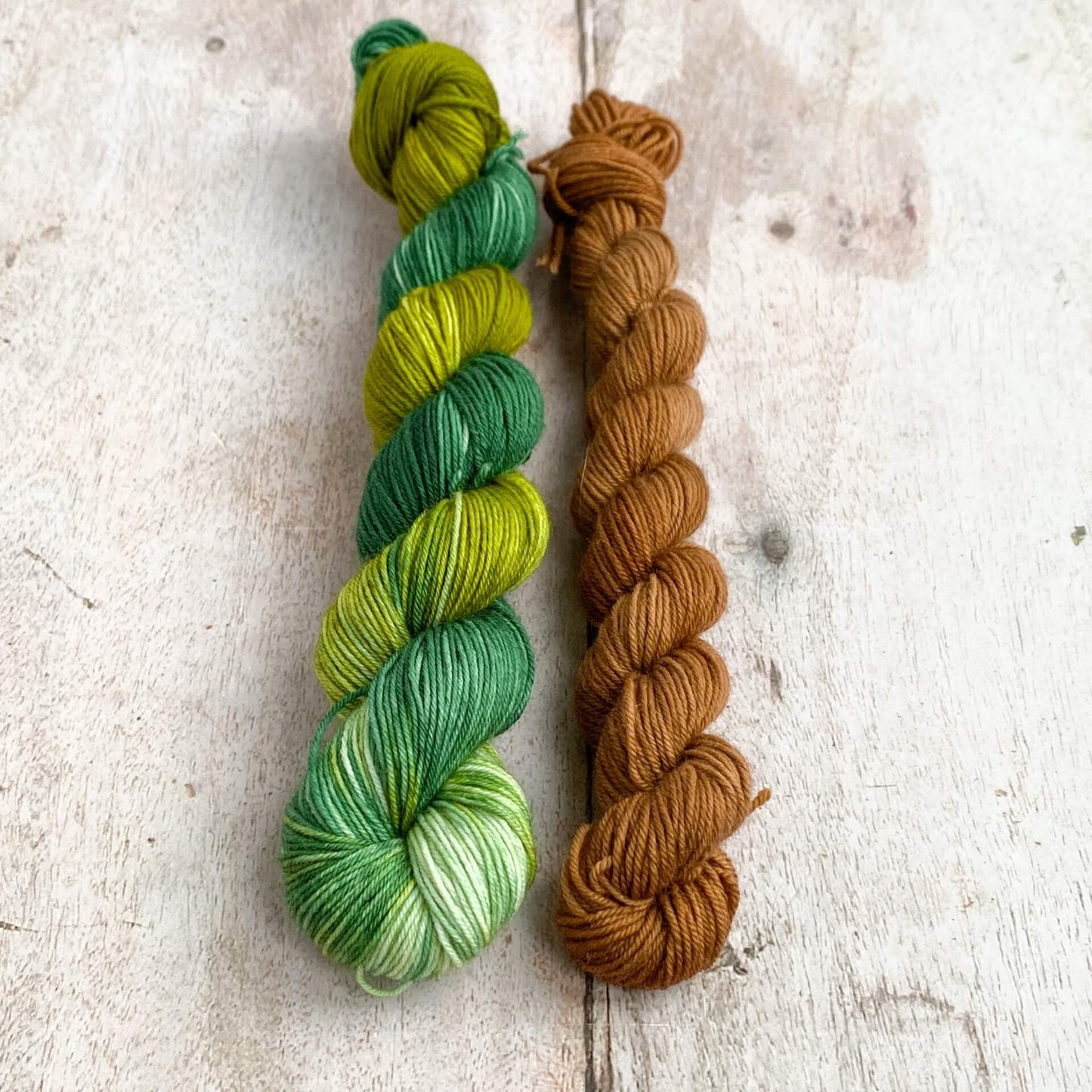 Two skeins of yarn hand dyed to look like a wintery fir tree sit on a wooden table. 