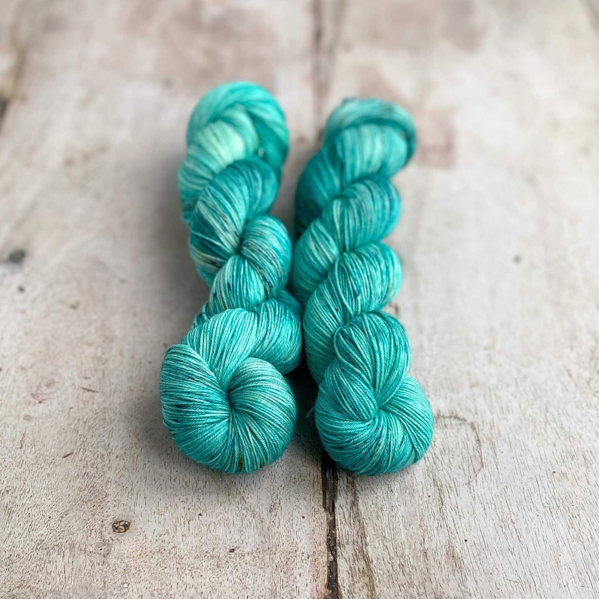 Two skeins of aqua blue tonal yarn sit on a wooden table. 