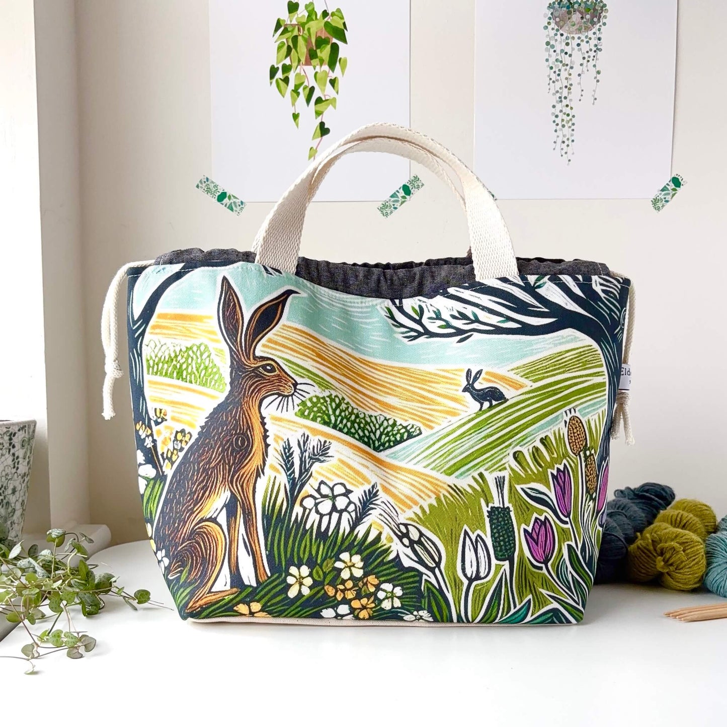 Fabric bag with nature-themed design featuring animals and plants on a white surface.