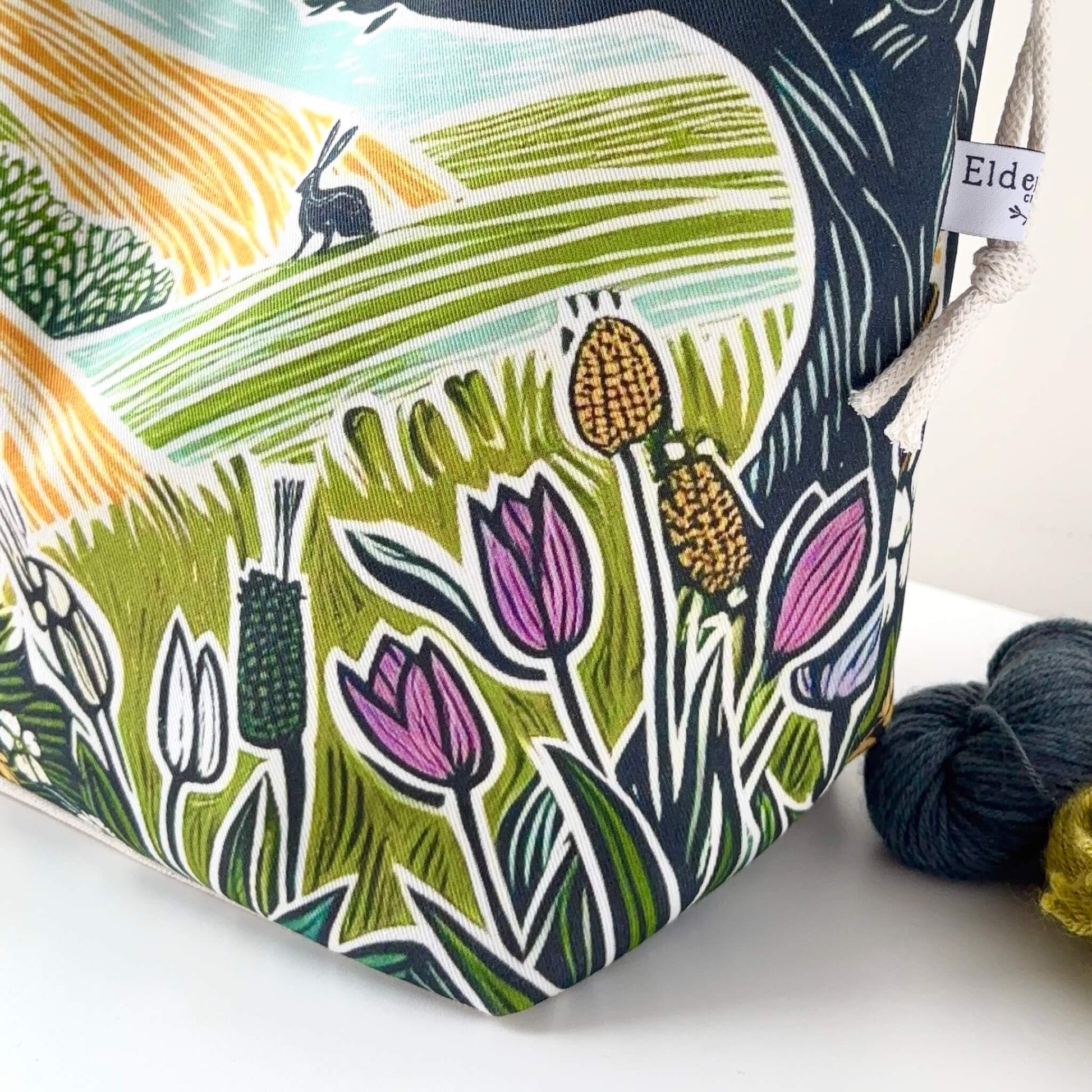 Fabric pouch with nature-themed design featuring flowers and a rabbit, next to yarn balls.