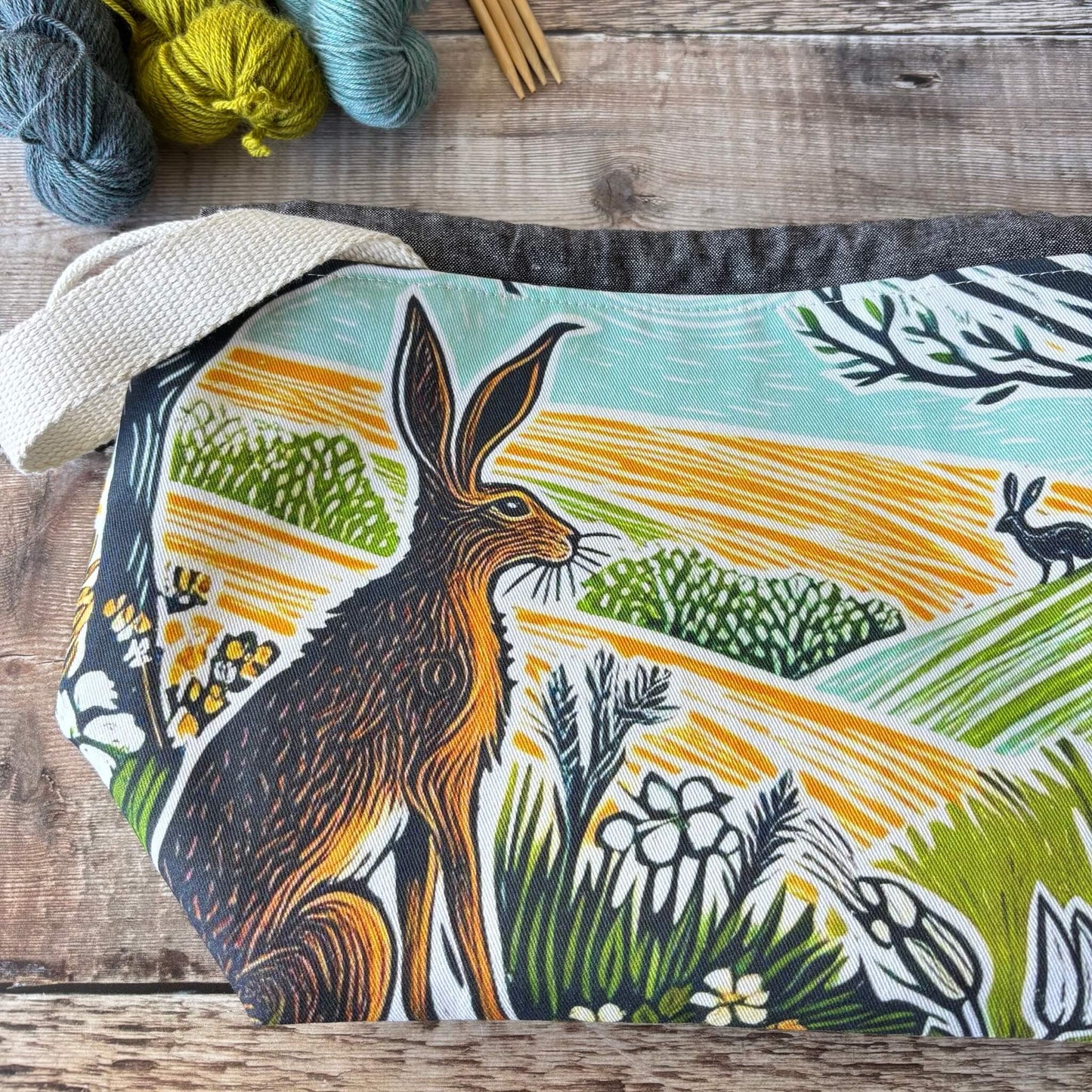 Project bag with a hare design on a wooden surface with yarn on the side.