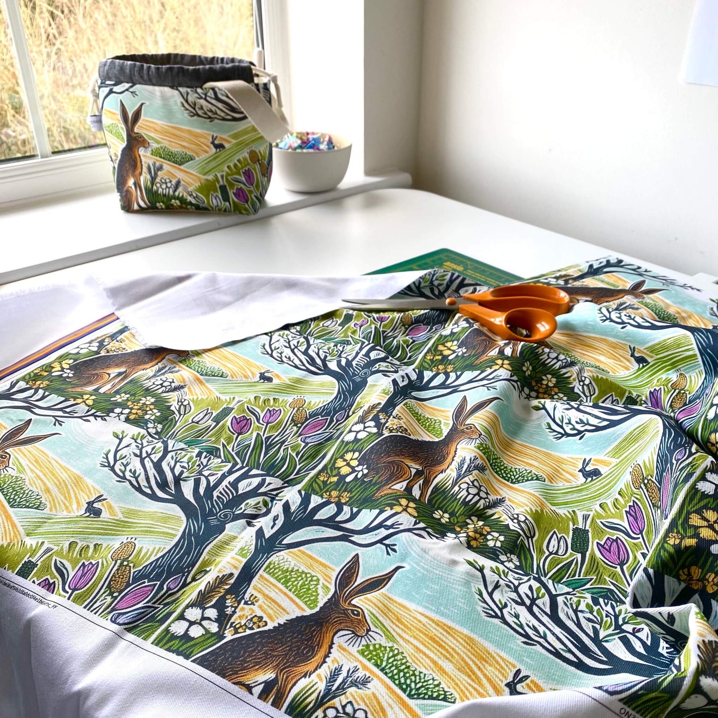 Fabric with nature-themed design featuring animals and trees on a table with scissors.