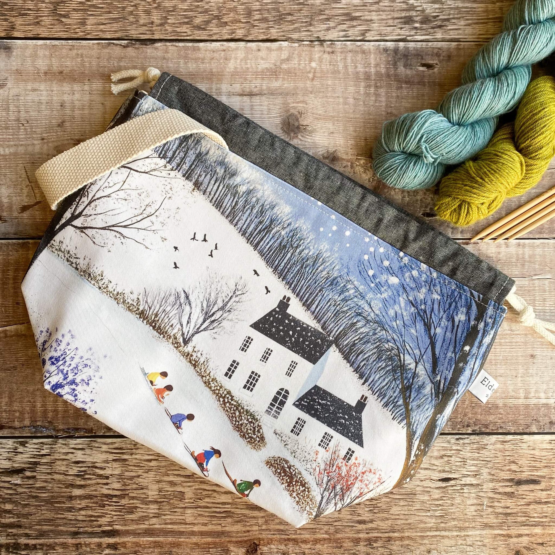 Fabric pouch with winter scene design on a wooden surface with yarn and knitting needles.