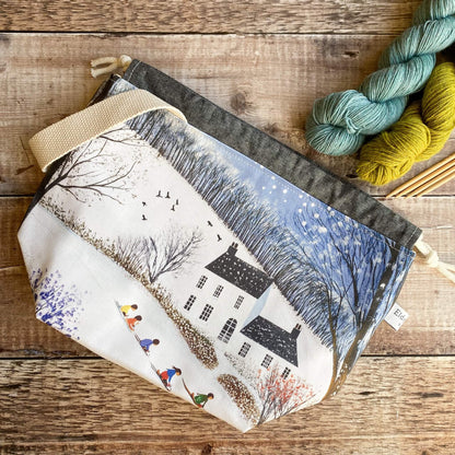 Fabric pouch with winter scene design on a wooden surface with yarn and knitting needles.