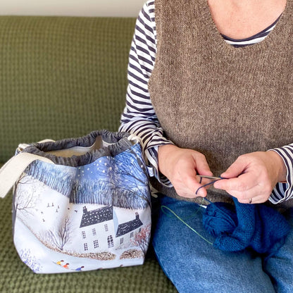 Person knitting with yarn and a winter themed project bag on a green couch