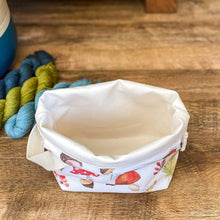 Load image into Gallery viewer, An empty project is sitting on a wooden floor in front of three skeins of yarn. We can see inside the project bag which is empty. 
