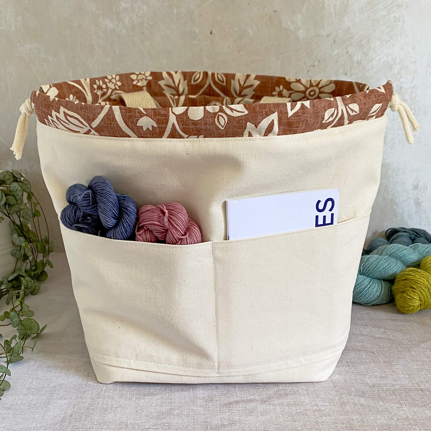 Interior view of a large sized knitting and crochet project bag, highlighting pockets on one side for storing knitting or crochet patterns, a notebook, pen, needles, hooks, and other crafting accessories. The interior is lined with durable natural-colored canvas.