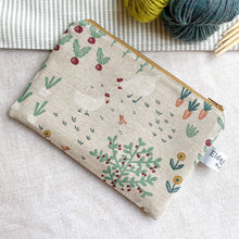 Load image into Gallery viewer, A small zipped pouch intended to be used for knitting notions lies on a table top next to two skeins of yarn and some wooden knitting needles. On the front of the pouch we can see some chickens, a bird, some beetroot and carrots, all printed in a whimsical style. 