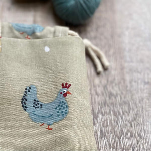 A close up of a knitting project bag. A blue chicken looks at the camera in a cheeky way.