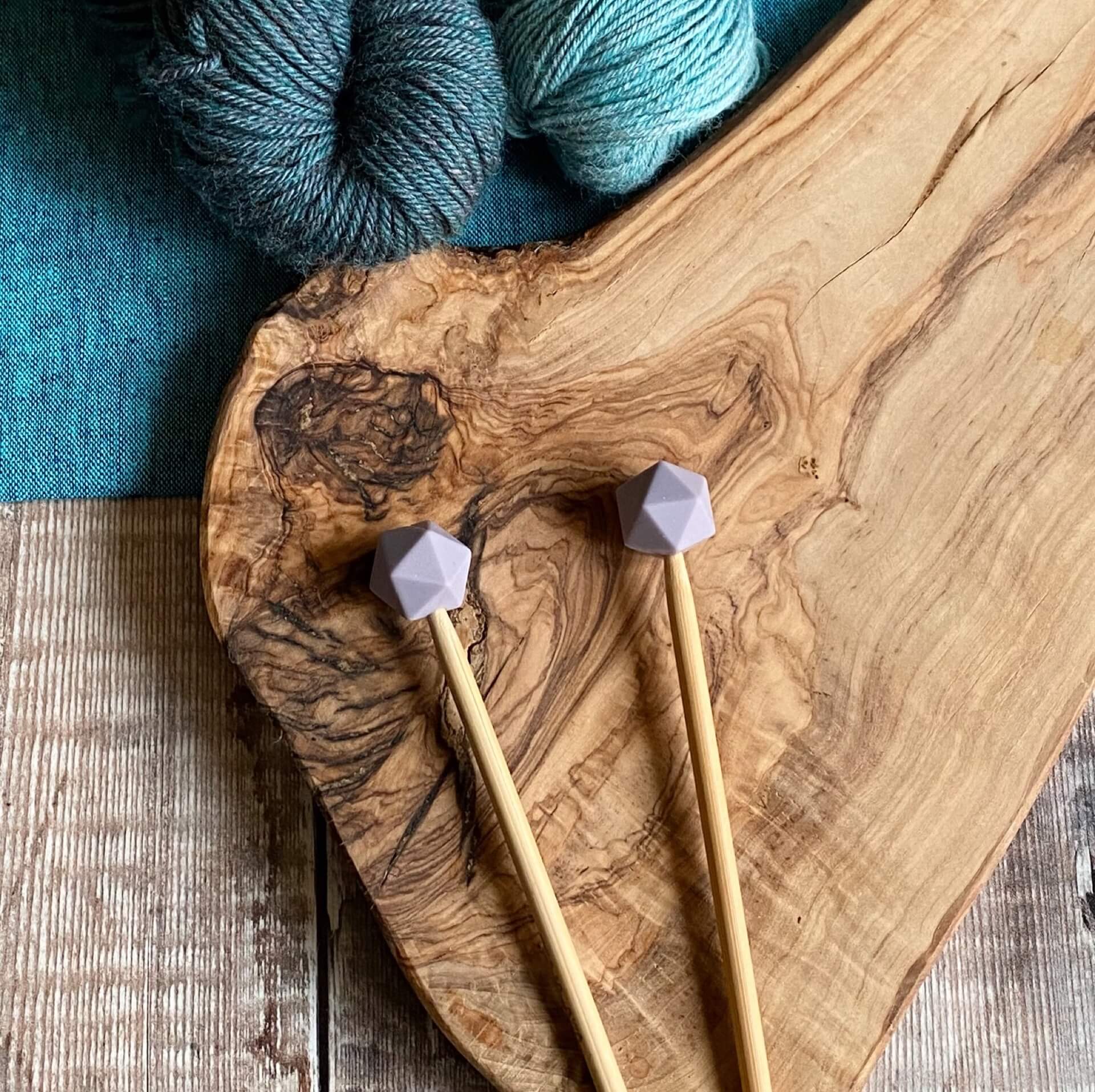 Mulberry needle protectors to stop stitches escaping from knitting needles. A pair sit on a wooden table attached to knitting needles. 