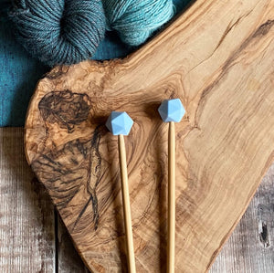 Robins Egg needle protectors to stop stitches escaping from knitting needles. A pair sit on a wooden table attached to knitting needles.