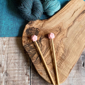 Rose needle protectors to stop stitches escaping from knitting needles. A pair sit on a wooden table attached to knitting needles. 