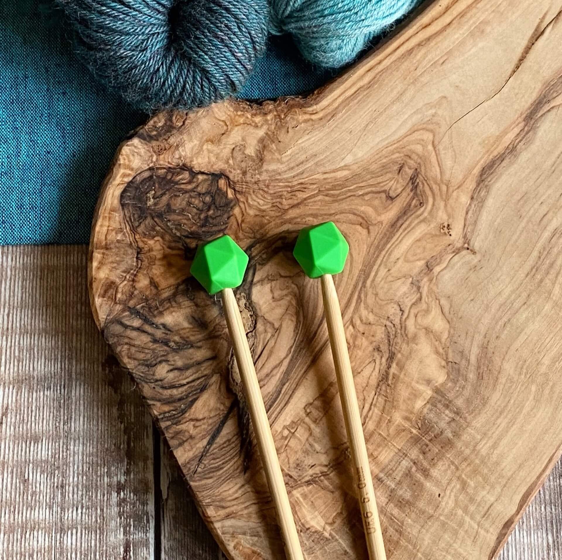 Summer Green needle protectors to stop stitches escaping from knitting needles. A pair sit on a wooden table attached to knitting needles. 