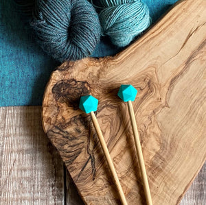  Turquoise needle protectors to stop stitches escaping from knitting needles. A pair sit on a wooden table attached to knitting needles. 