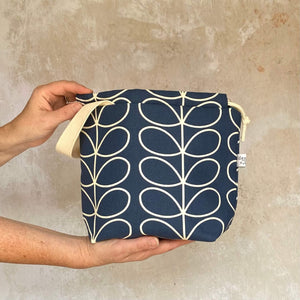 A handmade project bag in navy Orla Kiely fabric is held in front of a plastered wall.