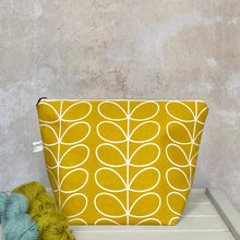 Load image into Gallery viewer, A zippered pouch sits on a bench next to some yarn. The bag is handmade from a cheerful sunshine yellow Orla Kiely fabric and is intended for use as a knitting project bag. 