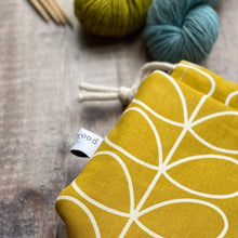 Load image into Gallery viewer, A close up of a knitting project bag in a cheerful yellow Orla Kiely print. The close up shows the quality of the fabric and one side of the Eldenwood Craft logo. 