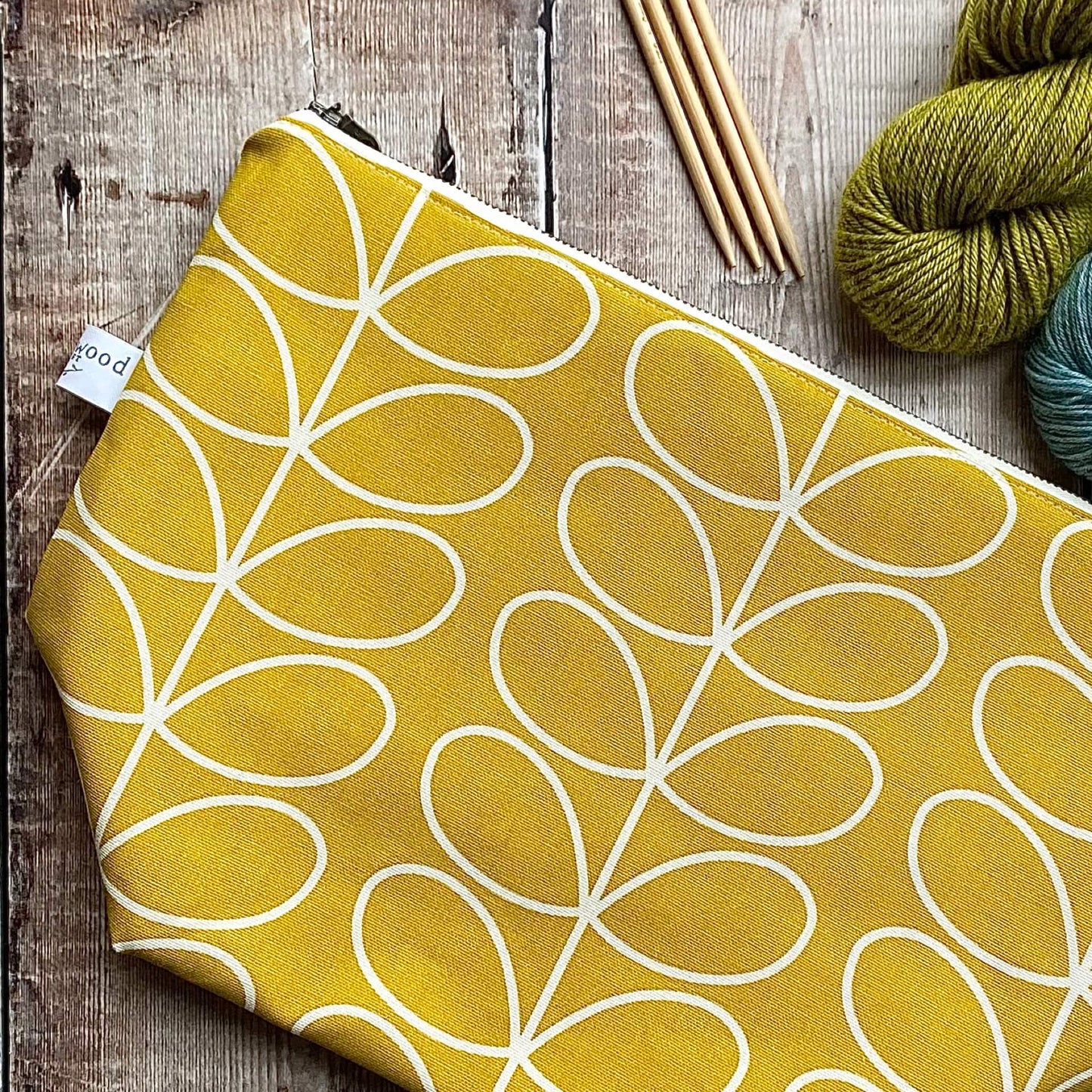 A sunshine yellow knitting project bag sits on a wooden table next to some skeins of yarn. 