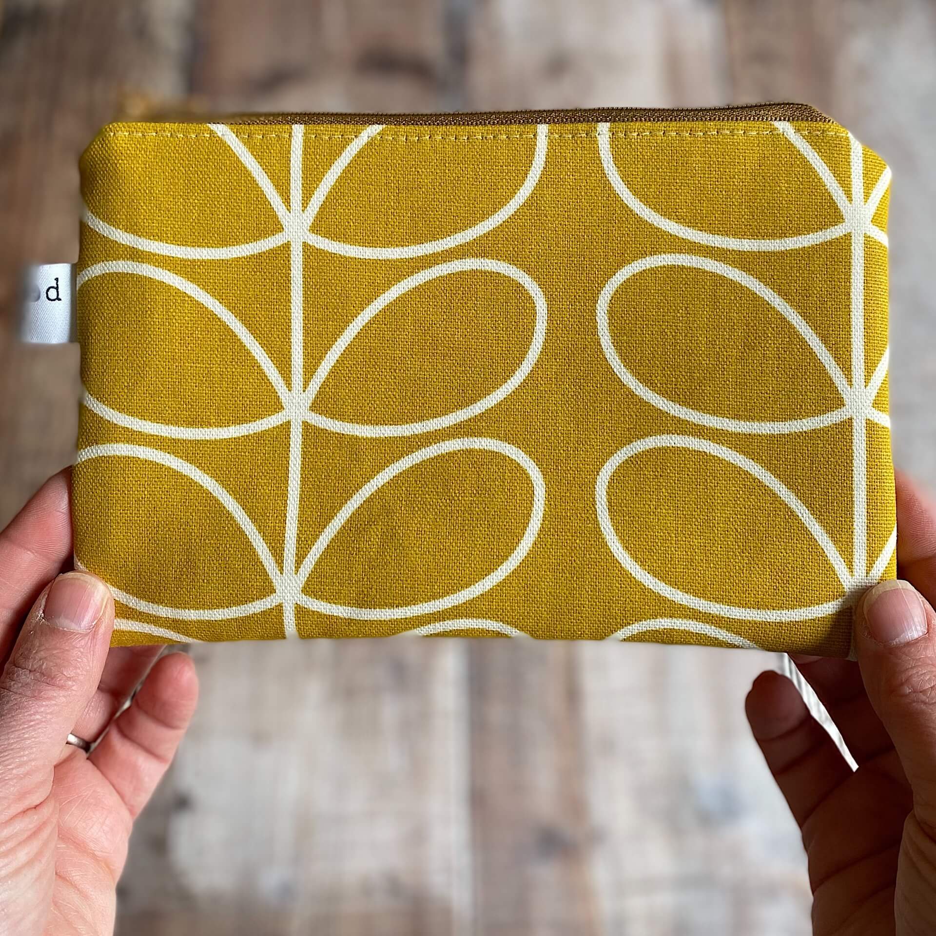 A cheerful yellow notions pouch is held up in front of a wooden table.