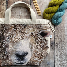 Load image into Gallery viewer, A large knitting project bag lies on a wooden table next to some yarn. From the bag fabric a large sheep face stares out. 