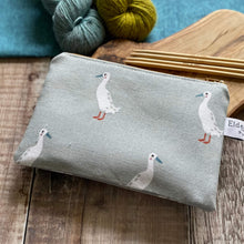 Load image into Gallery viewer, A small zippered pouch for knitting notions, which features some waddling runner ducks, sits on a wooden table next to two skeins of yarn, one blue the other green, and some knitting needles. The pouch has been hand made by Eldenwood Craft. 